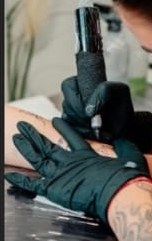 Tätowierer bei der Arbeit mit schwarzen Handschuhen